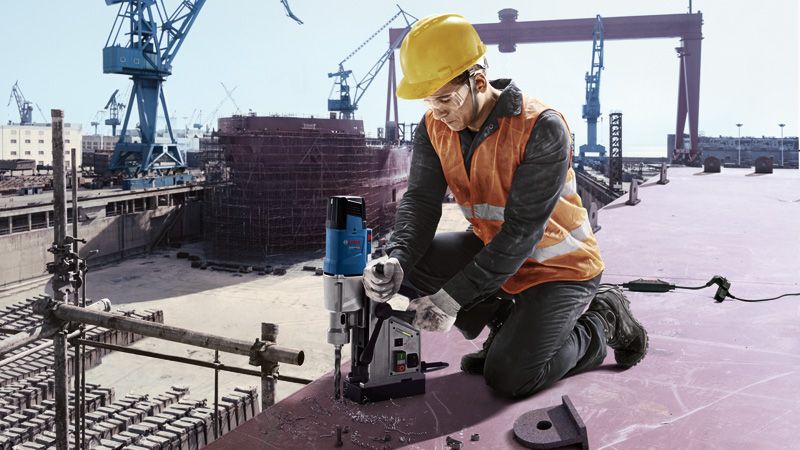 บุคคลที่สวมอุปกรณ์ด้านความปลอดภัยกำลังใช้งานสว่านแกนแม่เหล็กในไซต์ก่อสร้าง