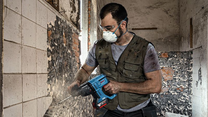 บุคคลที่สวมอุปกรณ์ด้านความปลอดภัยกำลังถอดกระเบื้องจากผนังโดยใช้เครื่องมือไฟฟ้า.