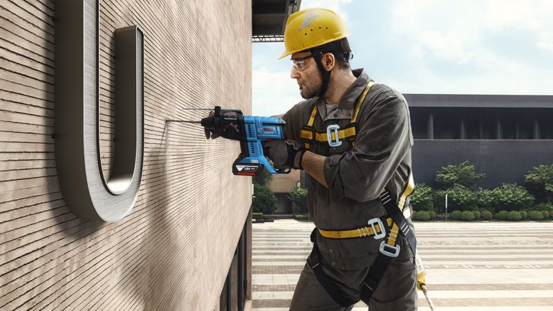 บุคคลที่สวมอุปกรณ์ความปลอดภัยเจาะเข้าไปในผนังอาคารในขณะที่ถูกแขวนอยู่.