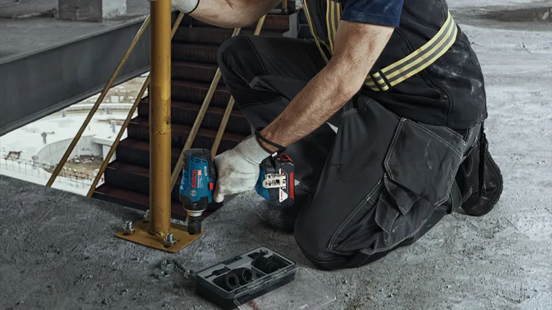 บุคคลที่สวมอุปกรณ์ด้านความปลอดภัยกำลังขันสลักเกลียวบนเสาโลหะโดยใช้ประแจกระแทกไร้สาย.