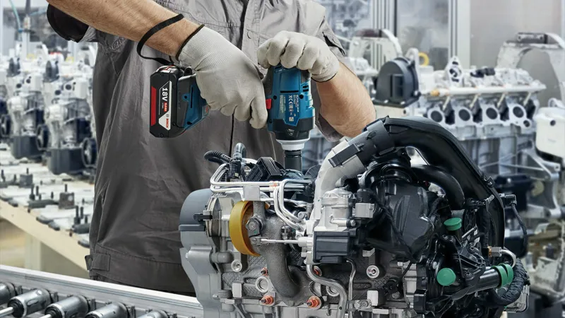 บุคคลที่สวมอุปกรณ์ด้านความปลอดภัยใช้ประแจกระแทกไร้สายกับชุดเครื่องยนต์.