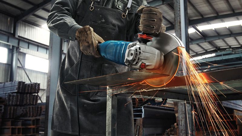 ผู้ที่สวมอุปกรณ์ป้องกันความปลอดภัยตัดแผ่นโลหะด้วยเครื่องเจียรขนาดใหญ่ มีประกายไฟกระเด็นออกมา.