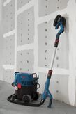 เครื่องขัดผนังแบบ Drywall เชื่อมต่อกับเครื่องดูดฝุ่นโดยวางพิงกับผนังที่ยังไม่เสร็จ