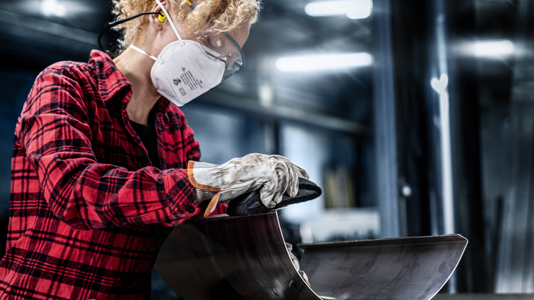 บุคคลที่สวมอุปกรณ์ความปลอดภัยกำลังขัดแผ่นโลหะโค้ง