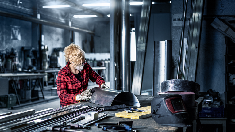 บุคคลที่สวมอุปกรณ์ความปลอดภัยกำลังตรวจสอบแผ่นโลหะโค้งในโรงงาน