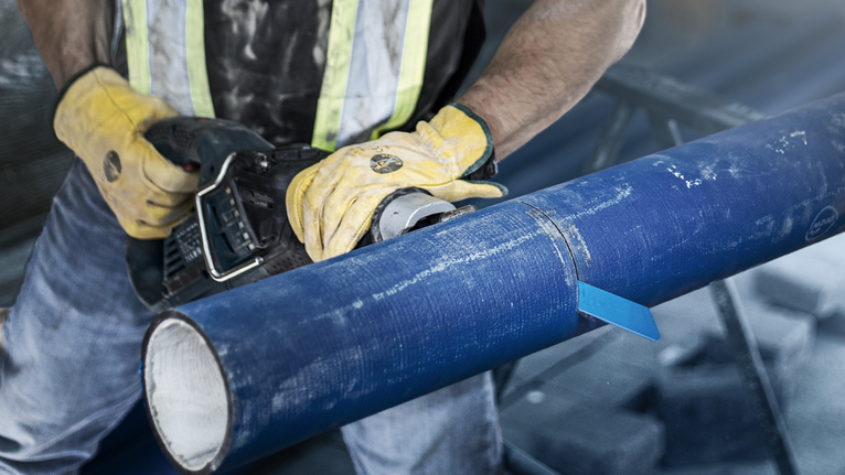 บุคคลที่สวมอุปกรณ์ความปลอดภัยตัดผ่านท่อสีน้ำเงินขนาดใหญ่ด้วยเครื่องมือไฟฟ้า