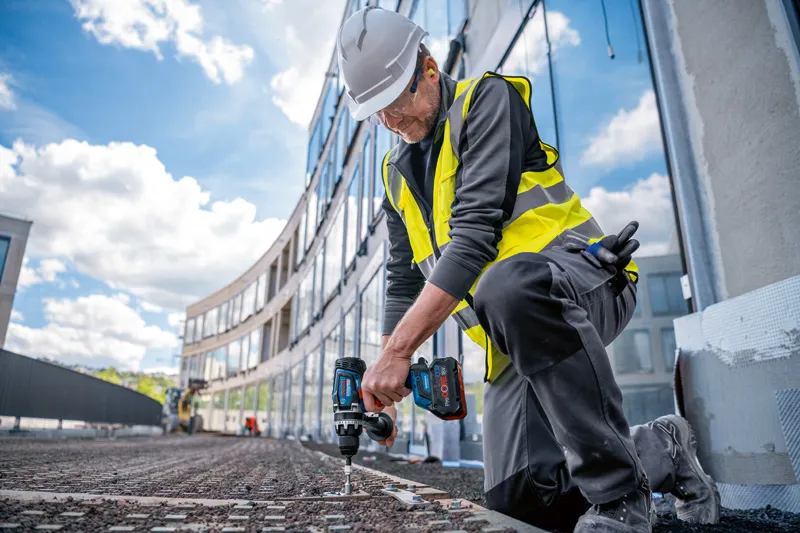 บุคคลที่สวมอุปกรณ์ด้านความปลอดภัยใช้สว่านไขควงไร้สายในพื้นที่ก่อสร้าง.
