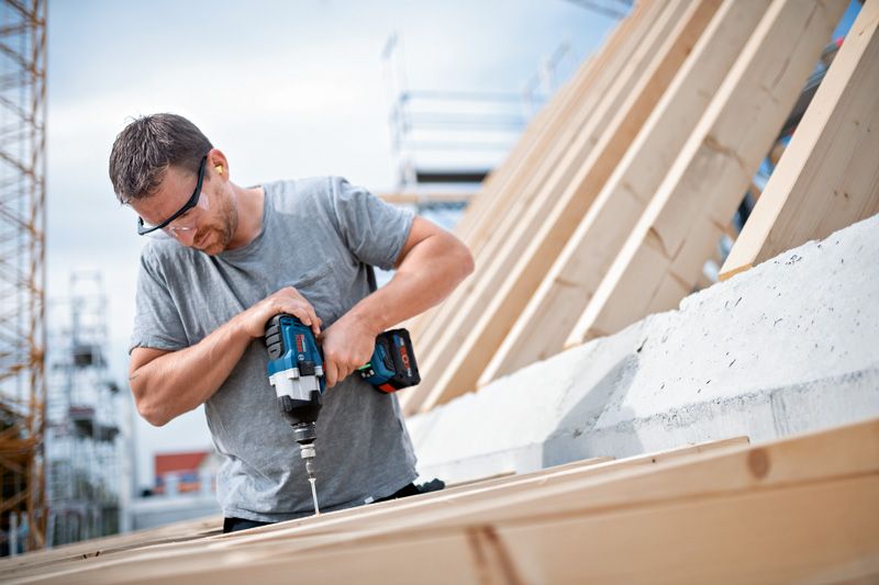 บุคคลที่สวมอุปกรณ์ด้านความปลอดภัยใช้ประแจกระแทกไร้สายในการขันสกรูเข้าไปในไม้.