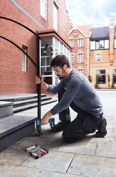 ผู้ที่สวมอุปกรณ์ป้องกันความปลอดภัยกำลังเจาะขั้นบันไดหินเพื่อติดตั้งราวจับโลหะ.