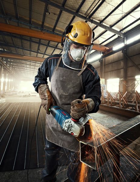 บุคคลที่สวมอุปกรณ์ความปลอดภัยกำลังบดโลหะ ทำให้เกิดประกายไฟสว่างในโรงงาน.
