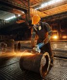 บุคคลที่สวมอุปกรณ์ความปลอดภัยกำลังบดท่อโลหะขนาดใหญ่ จึงทำให้เกิดประกายไฟ.