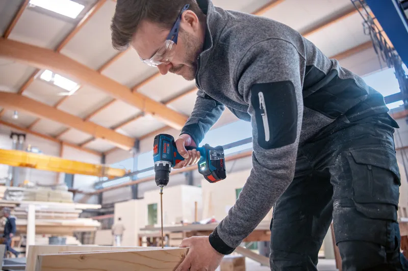 บุคคลที่สวมอุปกรณ์ด้านความปลอดภัยกำลังเจาะไม้โดยใช้เครื่องมือไฟฟ้าไร้สาย.