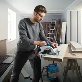 บุคคลที่สวมอุปกรณ์ความปลอดภัยกำลังตัดไม้ด้วยเลื่อยวงเดือนไร้สายในโรงงาน.