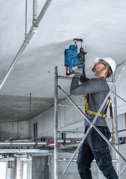 บุคคลที่สวมอุปกรณ์ด้านความปลอดภัยเจาะเพดานคอนกรีตขณะยืนอยู่บนนั่งร้าน.