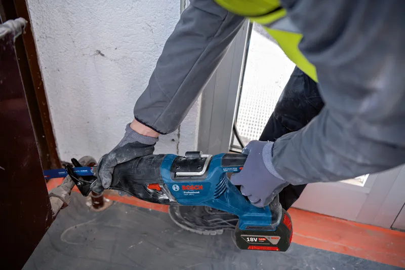 บุคคลที่สวมอุปกรณ์ด้านความปลอดภัยใช้เลื่อยตัดโลหะบริเวณใกล้กรอบประตู.