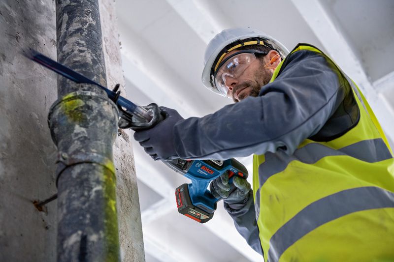 บุคคลที่สวมอุปกรณ์ความปลอดภัยกำลังตัดท่อโลหะด้วยเลื่อยตัดโลหะแบบลูกสูบ.