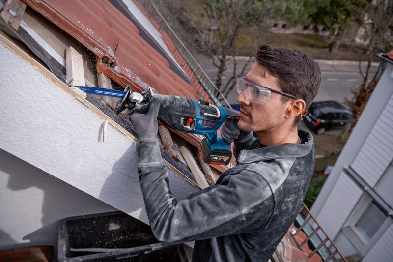 บุคคลที่สวมอุปกรณ์ด้านความปลอดภัยใช้เลื่อยตัดไม้บนหลังคา.