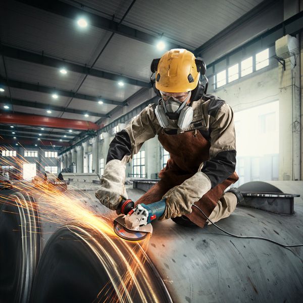 บุคคลที่สวมอุปกรณ์ด้านความปลอดภัยกำลังบดโลหะ ทำให้เกิดประกายไฟในสถานประกอบการอุตสาหกรรม.