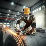 บุคคลที่สวมอุปกรณ์ด้านความปลอดภัยกำลังบดโลหะ ทำให้เกิดประกายไฟในสถานประกอบการอุตสาหกรรม.