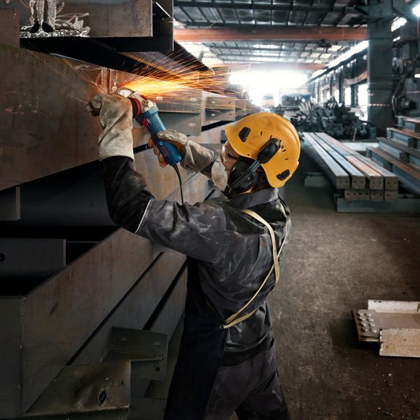 บุคคลที่สวมอุปกรณ์ป้องกันความปลอดภัยกำลังบดลำแสงโลหะ ทำให้เกิดประกายไฟสว่าง.