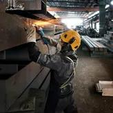 บุคคลที่สวมอุปกรณ์ป้องกันความปลอดภัยกำลังบดลำแสงโลหะ ทำให้เกิดประกายไฟสว่าง.