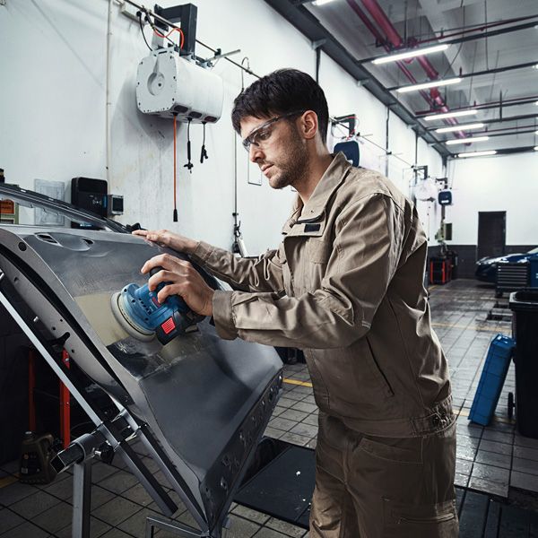 บุคคลที่สวมอุปกรณ์ความปลอดภัยกำลังขัดประตูรถด้วยเครื่องขัดไฟฟ้า.