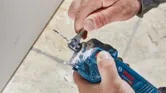 บุคคลกำลังปรับดอกเราเตอร์ drywall แบบไร้สายโดยใช้ประแจใกล้กับพื้นผิว drywall.