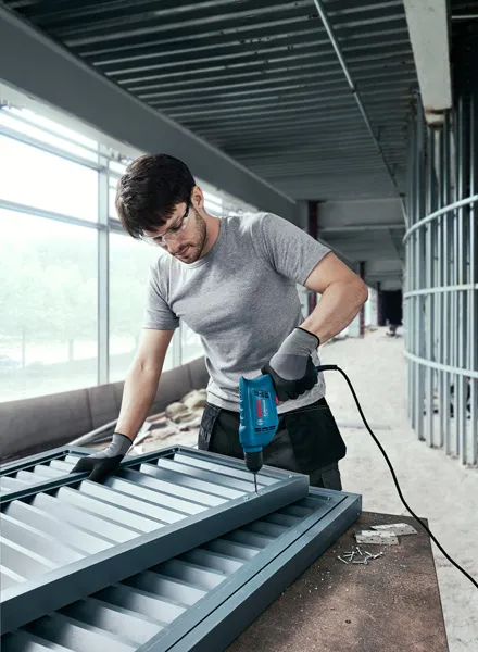 บุคคลที่สวมอุปกรณ์ความปลอดภัยกำลังเจาะสกรูเข้ากับโครงโลหะบนไซต์ก่อสร้าง.