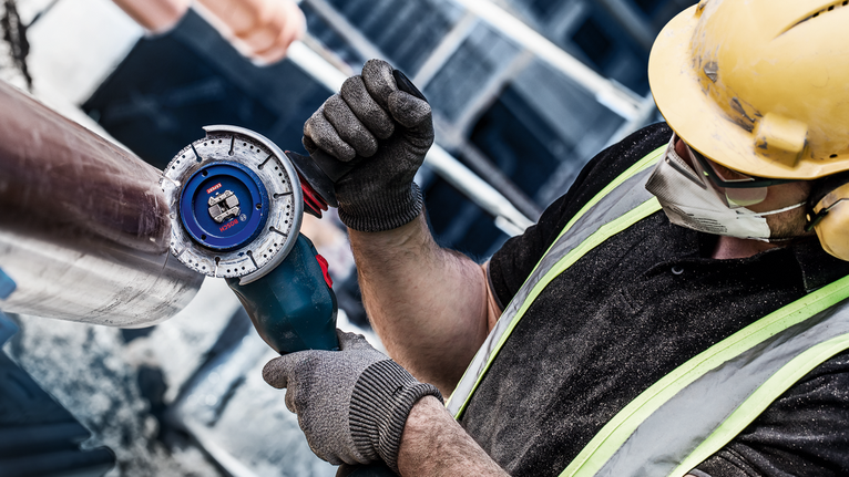 บุคคลที่สวมอุปกรณ์ความปลอดภัยใช้เครื่องเจียรตัดท่อโลหะ