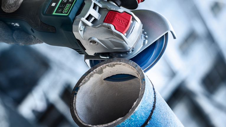 บุคคลที่สวมอุปกรณ์ความปลอดภัยใช้เครื่องเจียรตัดผ่านท่อโลหะ