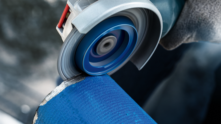 บุคคลที่สวมอุปกรณ์ความปลอดภัยกำลังเจียรท่อโลหะสีน้ำเงินด้วยเครื่องเจียรแบบมุม