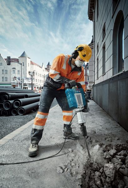 บุคคลที่สวมอุปกรณ์ความปลอดภัยทำลายทางเท้าด้วยเครื่องตัดกระแสไฟฟ้าบนถนนในเมือง.