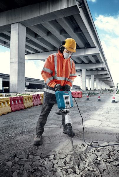 บุคคลที่สวมอุปกรณ์ด้านความปลอดภัยทำลายคอนกรีตด้วยเครื่องทำลายไฟฟ้าขนาดใหญ่กลางแจ้ง.