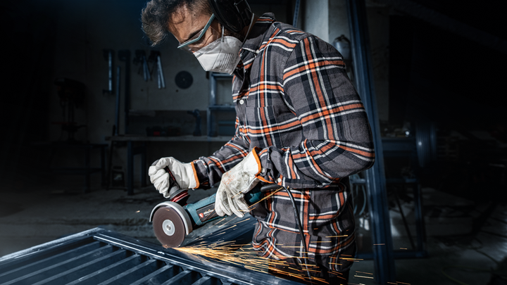 บุคคลที่สวมอุปกรณ์ความปลอดภัยทำการบดโลหะ ทำให้เกิดประกายไฟ