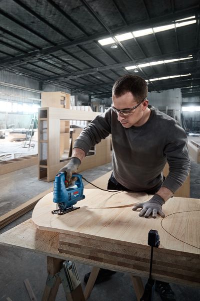 บุคคลที่สวมอุปกรณ์ความปลอดภัยใช้จิ๊กซอว์ตัดรูปทรงโค้งในไม้อัด.