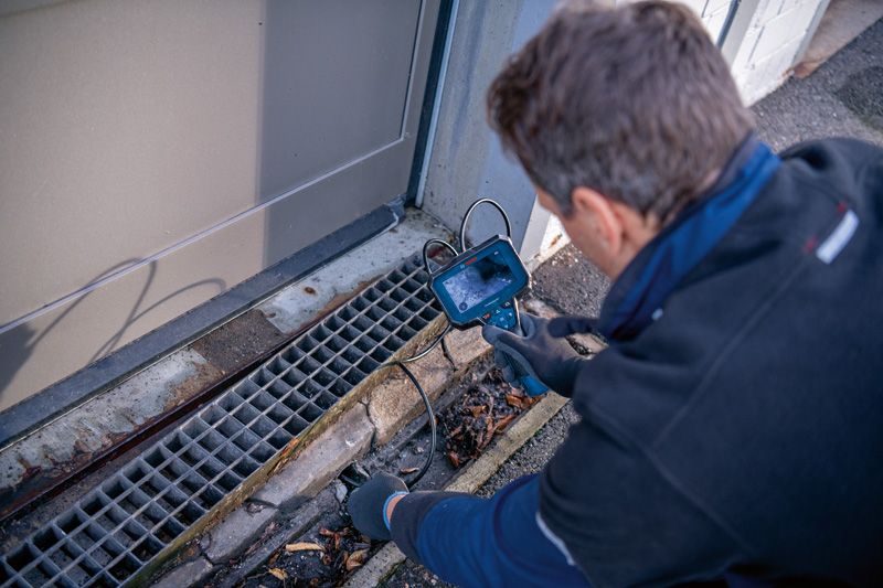 บุคคลที่สวมอุปกรณ์ด้านความปลอดภัยกำลังตรวจสอบท่อระบายน้ำโดยใช้กล้องตรวจสอบ.