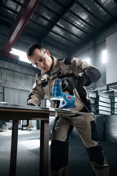 ผู้ที่สวมอุปกรณ์ด้านความปลอดภัยกำลังใช้เลื่อยจิ๊กซอว์ตัดโลหะในโรงงาน.