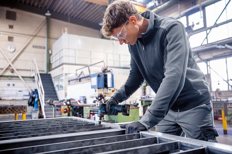 บุคคลที่สวมอุปกรณ์ด้านความปลอดภัยใช้เครื่องเจียรโรเตอรี่บนโครงโลหะ.