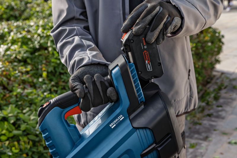 บุคคลที่สวมอุปกรณ์ด้านความปลอดภัยใส่แบตเตอรี่เข้าไปในเครื่องเป่าใบไม้ไร้สายกลางแจ้ง