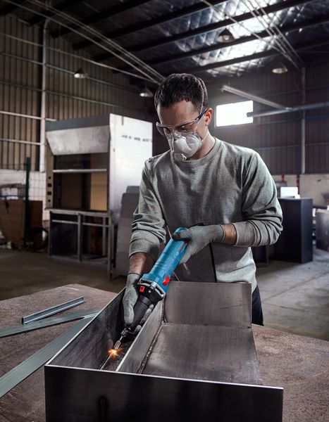 บุคคลที่สวมอุปกรณ์ความปลอดภัยกำลังบดโลหะภายในโรงงานอุตสาหกรรม.