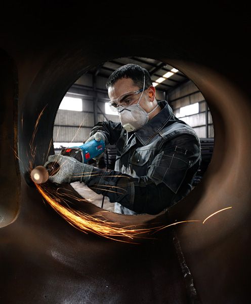 บุคคลที่สวมอุปกรณ์ด้านความปลอดภัยกำลังบดโลหะภายในท่อขนาดใหญ่ ทำให้เกิดประกายไฟ.