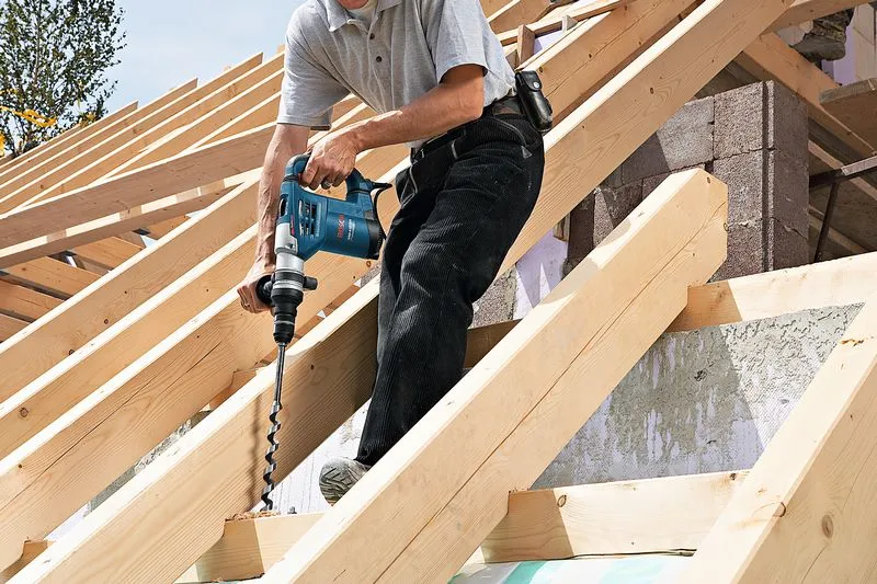 คนกำลังเจาะคานไม้บนโครงหลังคา โดยไม่สวมอุปกรณ์ป้องกันความปลอดภัย.