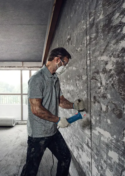 บุคคลที่สวมอุปกรณ์ด้านความปลอดภัยใช้เครื่องเจียรตัดเข้าไปในผนังคอนกรีต.