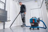 บุคคลที่สวมอุปกรณ์ด้านความปลอดภัยใช้เครื่องดูดฝุ่นแบบไร้สายเพื่อทำความสะอาดพื้นกระเบื้อง.