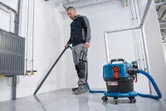 บุคคลที่สวมอุปกรณ์ด้านความปลอดภัยใช้เครื่องดูดฝุ่นแบบไร้สายเพื่อทำความสะอาดพื้นกระเบื้อง.
