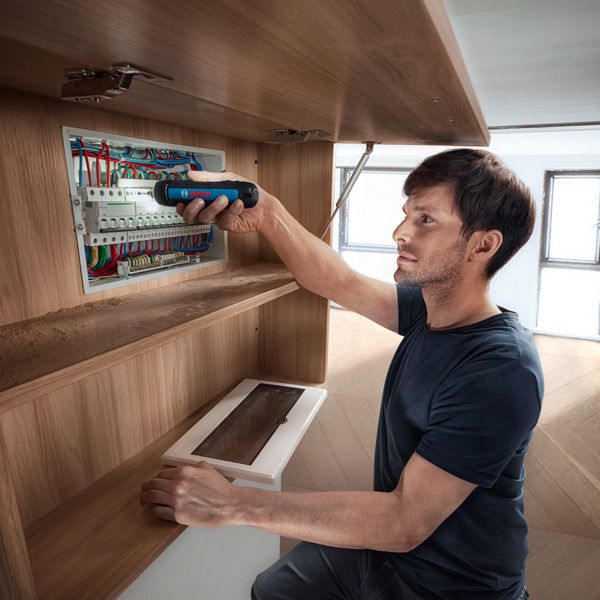 คนๆ หนึ่งกำลังยึดสายไฟในแผงไฟฟ้าโดยใช้ไขควงไร้สาย.