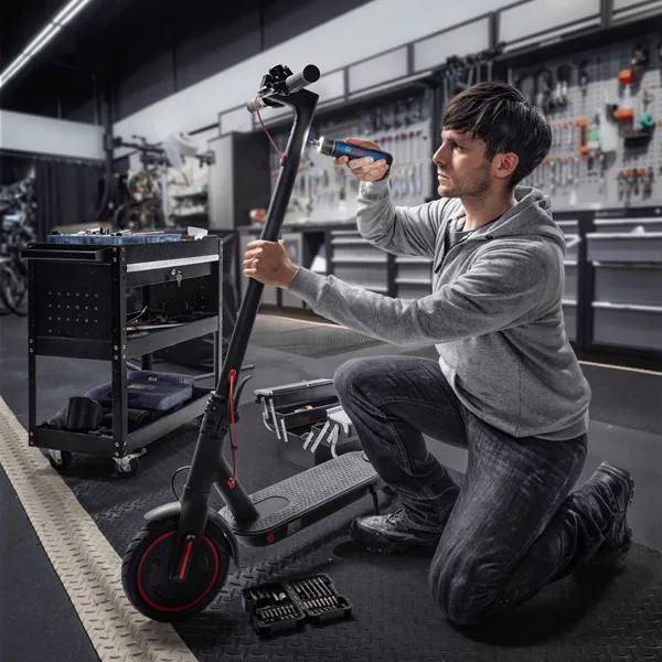 คนๆ หนึ่งคุกเข่าและใช้ไขควงไร้สายซ่อมสกู๊ตเตอร์ไฟฟ้า.