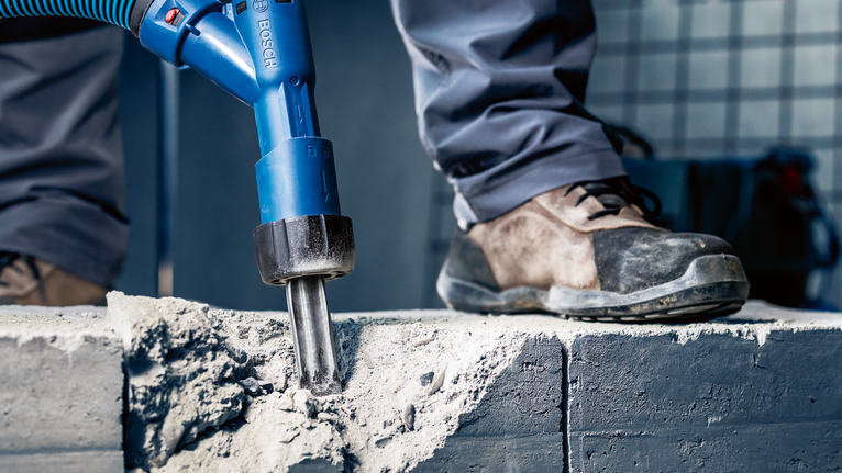 บุคคลที่สวมอุปกรณ์ความปลอดภัยทุบคอนกรีตด้วยเครื่องมือไฟฟ้า