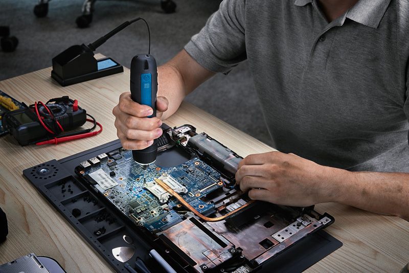 ผู้ใช้ไขควงไร้สายในการประกอบแล็ปท็อปบนโต๊ะทำงาน.