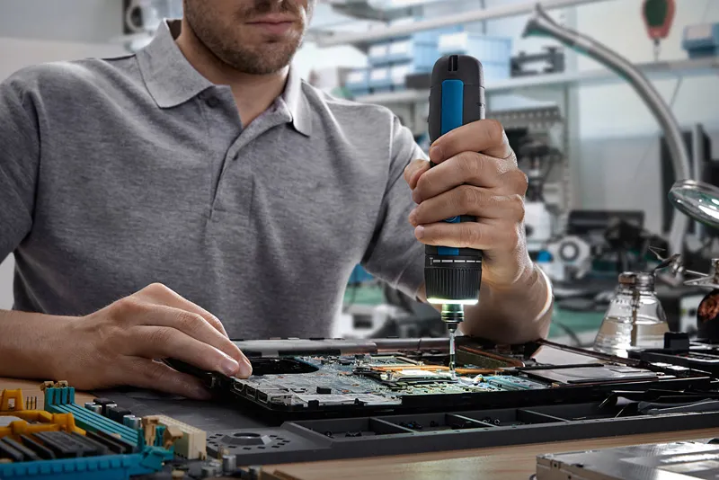 ผู้ใช้ไขควงไร้สายในการประกอบชิ้นส่วนอิเล็กทรอนิกส์บนแผงวงจร.